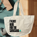 Natur Az I'M JUST HERE FOR THE SAVASANA - Prémium pamut shopper (PatentDuo) fehér színben, nagy fekete felirattal, kék jógaszőnyegen pihen napsütötte fapadlón, beige kulacs és feltekert jógamatrac mellett. natur színben